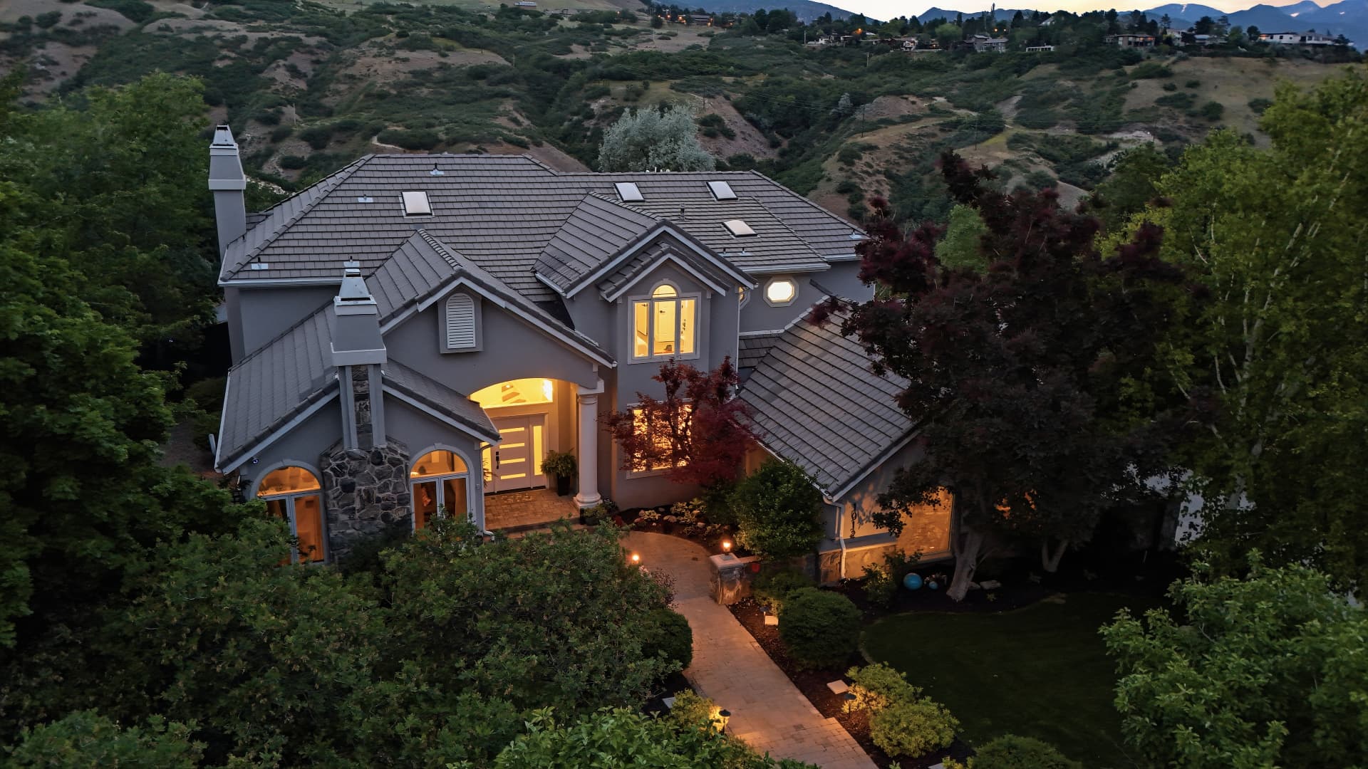 Aerial twilight view of a home on the Wasatch hillside with warm interior lights.
